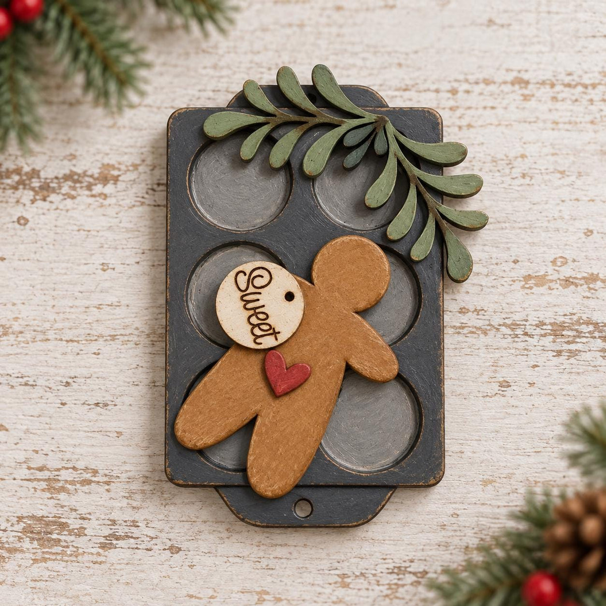 A wooden gingerbread man figure with a heart-shaped tag attached to it, placed on a wooden surface with pine branches and red berries in the background.