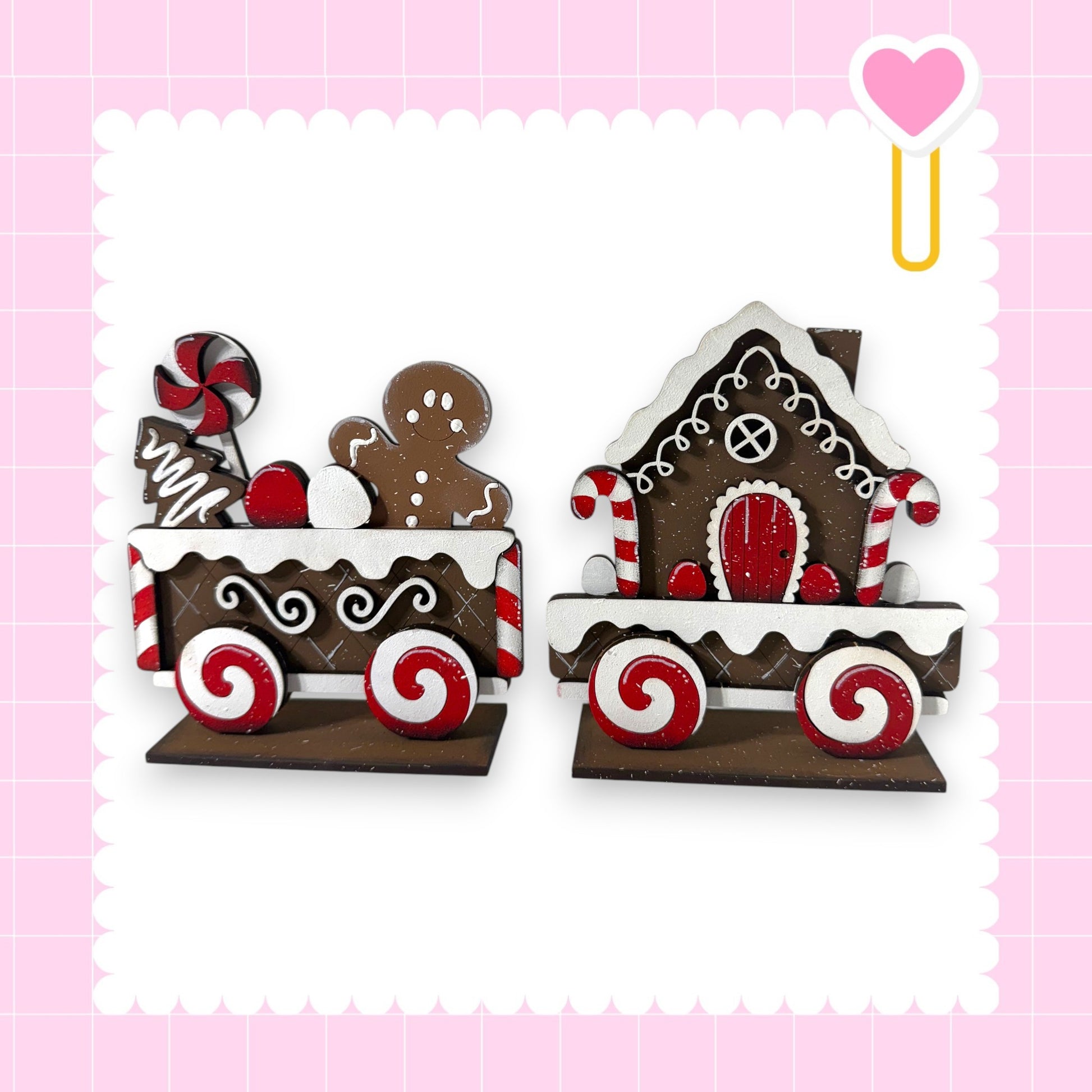 two wooden toy train cars, each decorated with candy and gingerbread houses, set against a pink background.