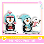two penguins and a snowman, all wearing winter accessories, with a pink and yellow border and text that reads "DIY WOOD PAINT KIT" and "IF WE CAN CREATE IT, YOU CAN MAKE IT!"