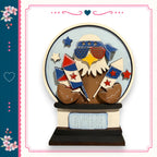 A decorative snow globe with an eagle wearing sunglasses and holding fireworks, surrounded by stars and flowers, with the text "Born in the USA" on the base.