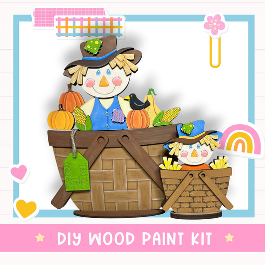A DIY wood paint kit featuring a scarecrow and a basket of produce, including pumpkins and corn, against a white background with a pink border.