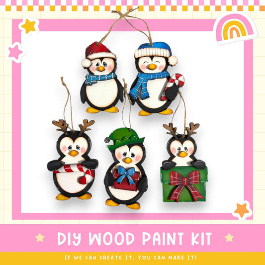 A DIY wood paint kit for creating ornaments in the shape of penguins, featuring five different penguin designs in various colors and styles.
