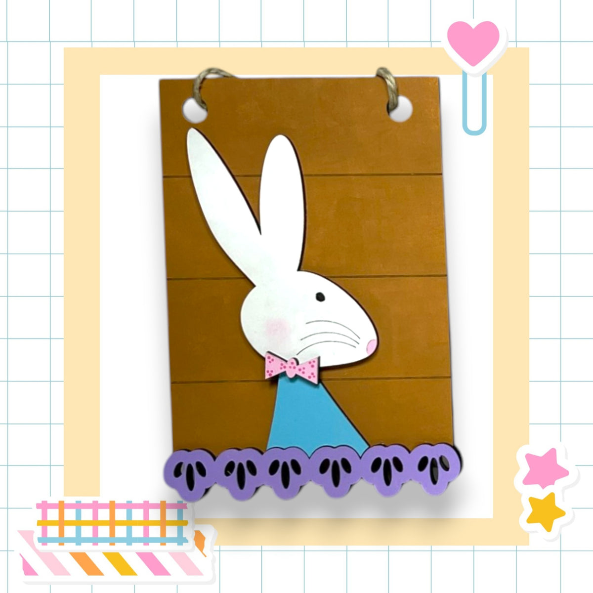 A paper craft of a white rabbit wearing a blue bow tie, with a brown background and purple paw prints, is displayed in a frame.