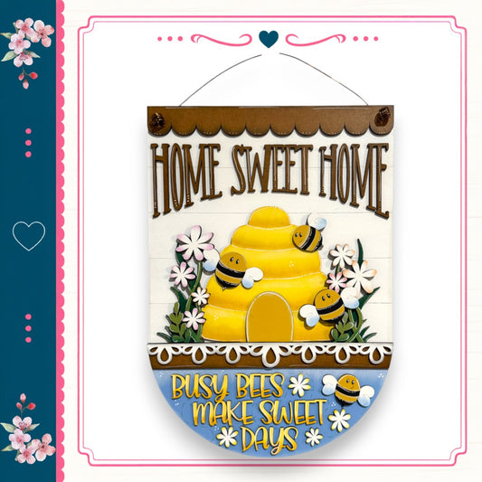 a decorative sign with a bee theme, displaying the text "HOME SWEET HOME" and "BUSY BEES MAKE SWEET DAYS" along with a bee illustration.