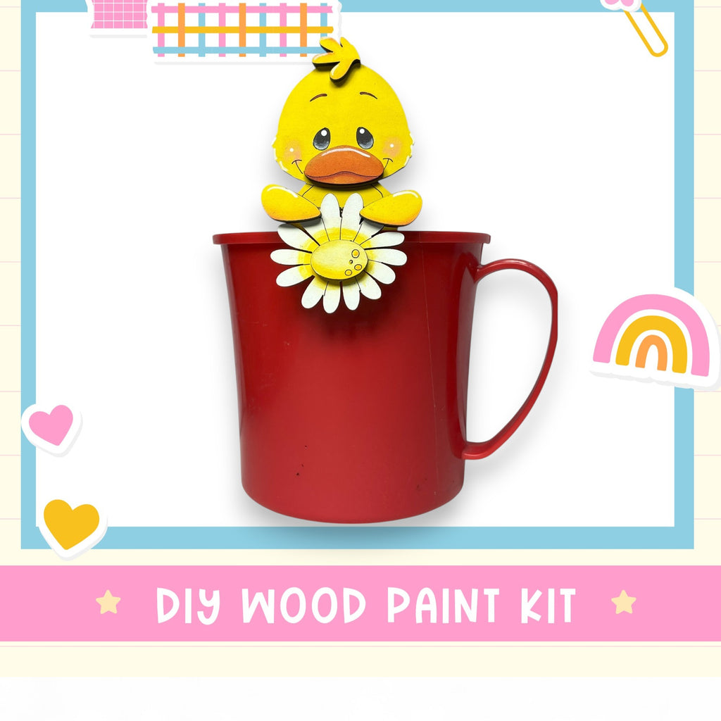 A red mug with a yellow duck figurine holding a white flower, surrounded by various colorful stickers and hearts, with the text "DIY WOOD PAINT KIT" below.