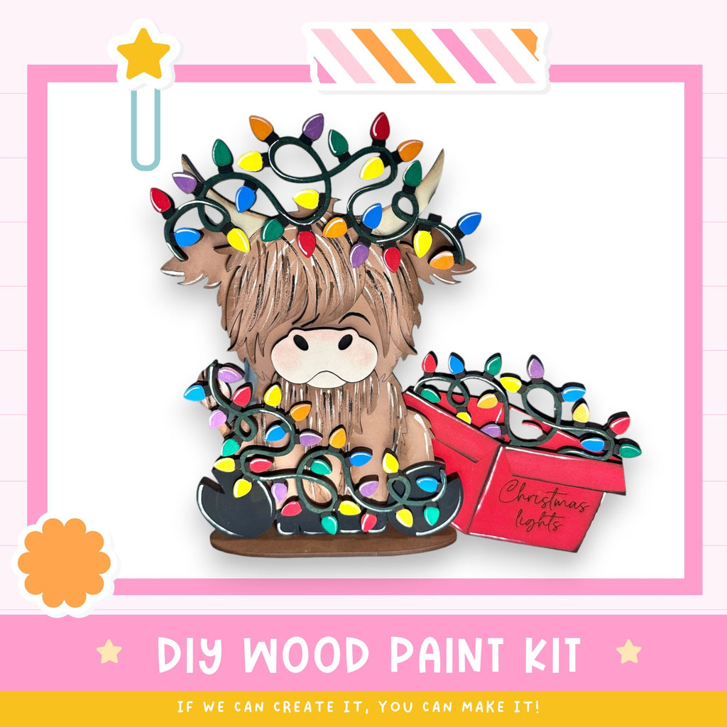 A wooden paint kit with a cartoon cow wearing a crown of colorful Christmas lights.