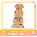 a DIY wood paint kit, with a wooden gnome figure as the main focus. The gnome is wearing a hat with a flower and has a heart-shaped bow around its neck. The kit appears to be made of wood and is designed for creating wooden figures.
