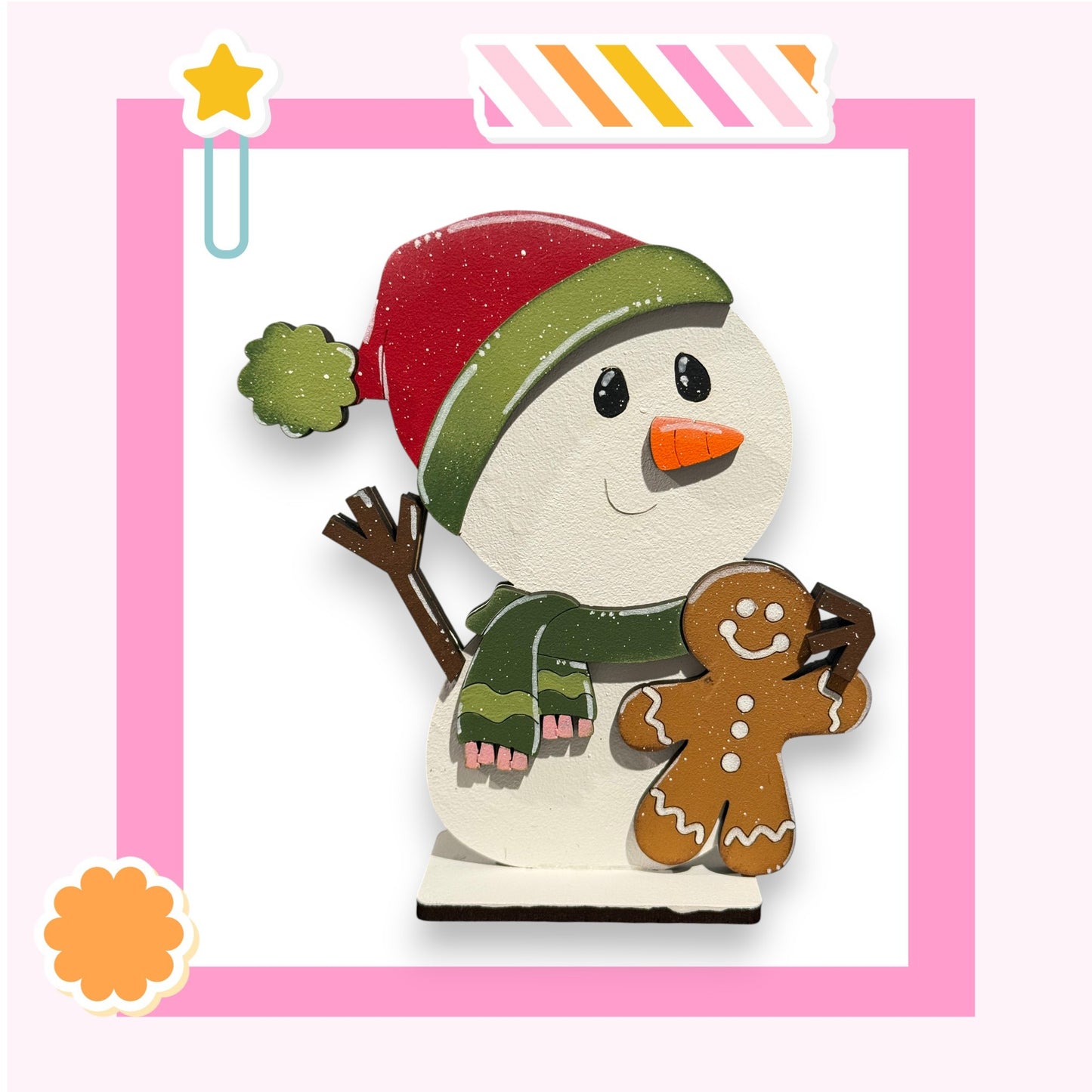 A cheerful snowman figure holding a gingerbread man figure, set against a pink background with a star decoration.