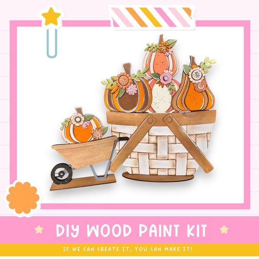 The image is a colorful illustration of a wooden basket filled with decorative pumpkins, accompanied by a wheelbarrow. The basket and wheelbarrow are set against a pink and white striped background.