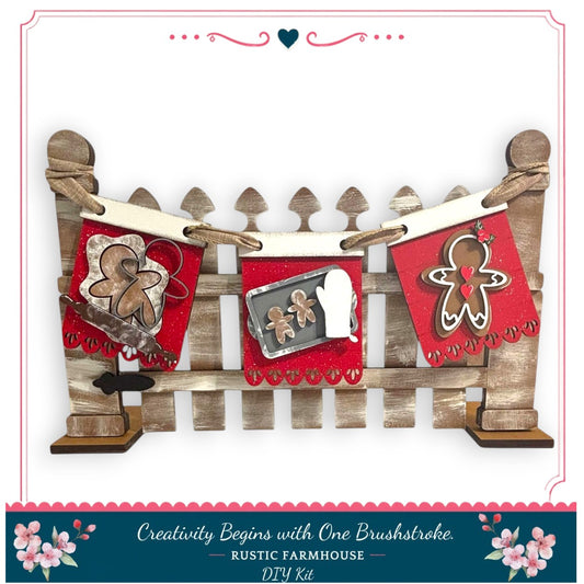 A rustic farmhouse-style DIY kit featuring a wooden fence with decorative elements such as gingerbread man and heart-shaped cutouts, along with a caption that reads "Creativity Begins with One Brushstroke - RUSTIC FARMHOUSE - DIY KIT".