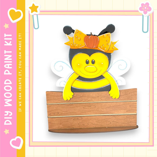 A cheerful cartoon bee wearing a yellow bow and sitting on a wooden plank.