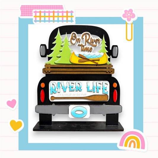 a black truck with a wooden bed, decorated with various objects related to river life, such as a canoe, pine trees, and a sign that says "On River Time".