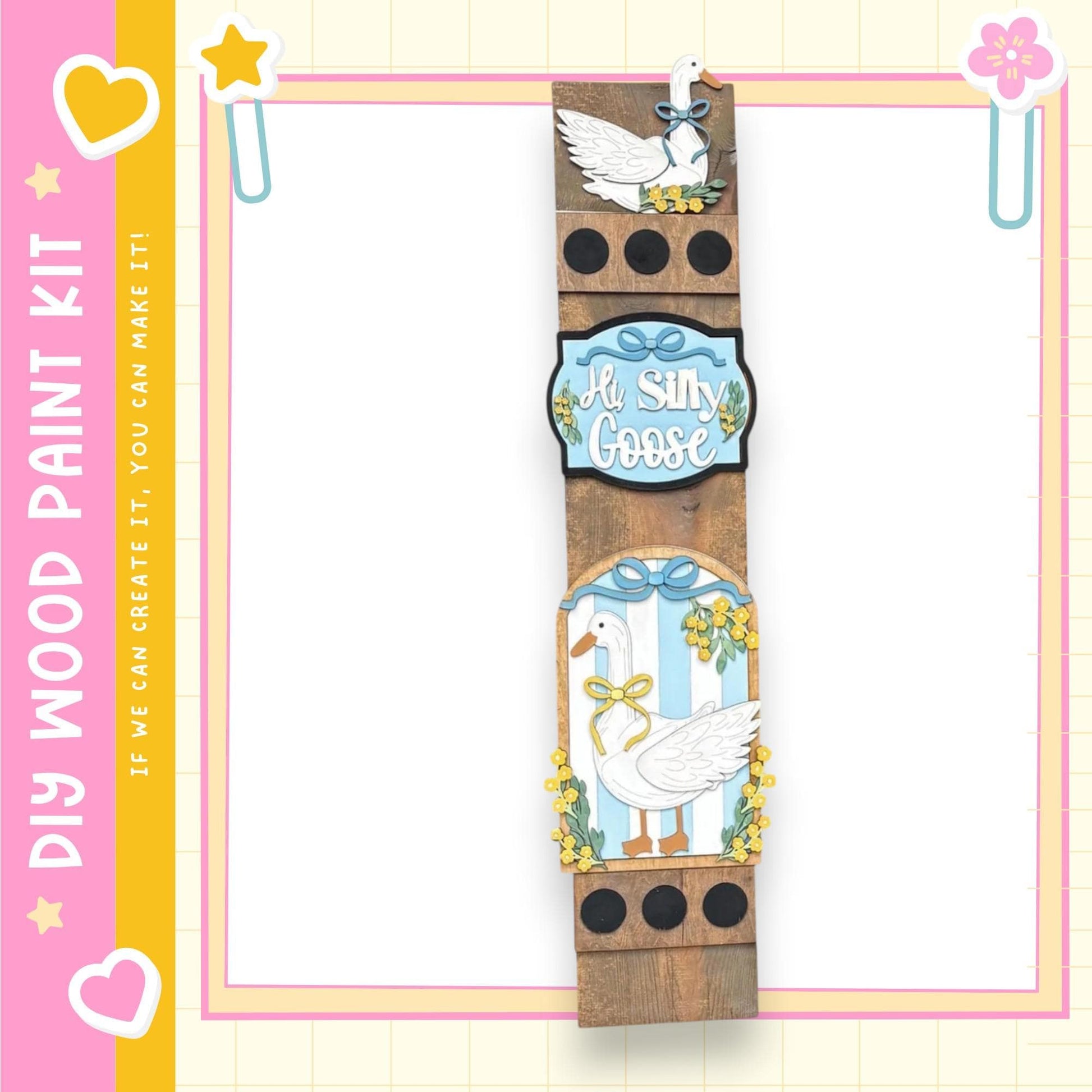 a wooden frame with a decorative design, including a white goose and yellow flowers. The frame is surrounded by a pink and yellow border, and there are decorative elements such as hearts and a star on the border.