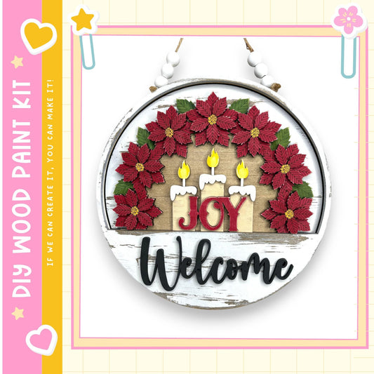 a circular wooden sign with a wreath of red poinsettia flowers and three lit candles, along with the word "Joy" written on it.