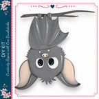 A cute gray bat with large eyes and a pink nose is hanging upside down from a branch, surrounded by a decorative border.