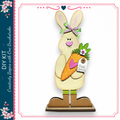 A wooden rabbit figurine holding a carrot and wearing a bow, standing on a wooden base.