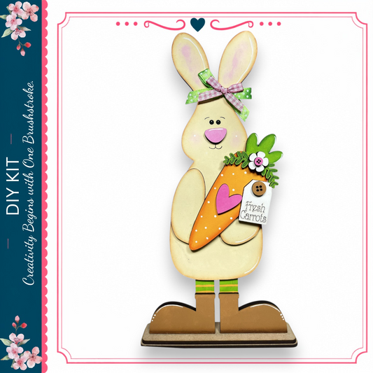 A wooden rabbit figurine holding a carrot and wearing a bow, standing on a wooden base.