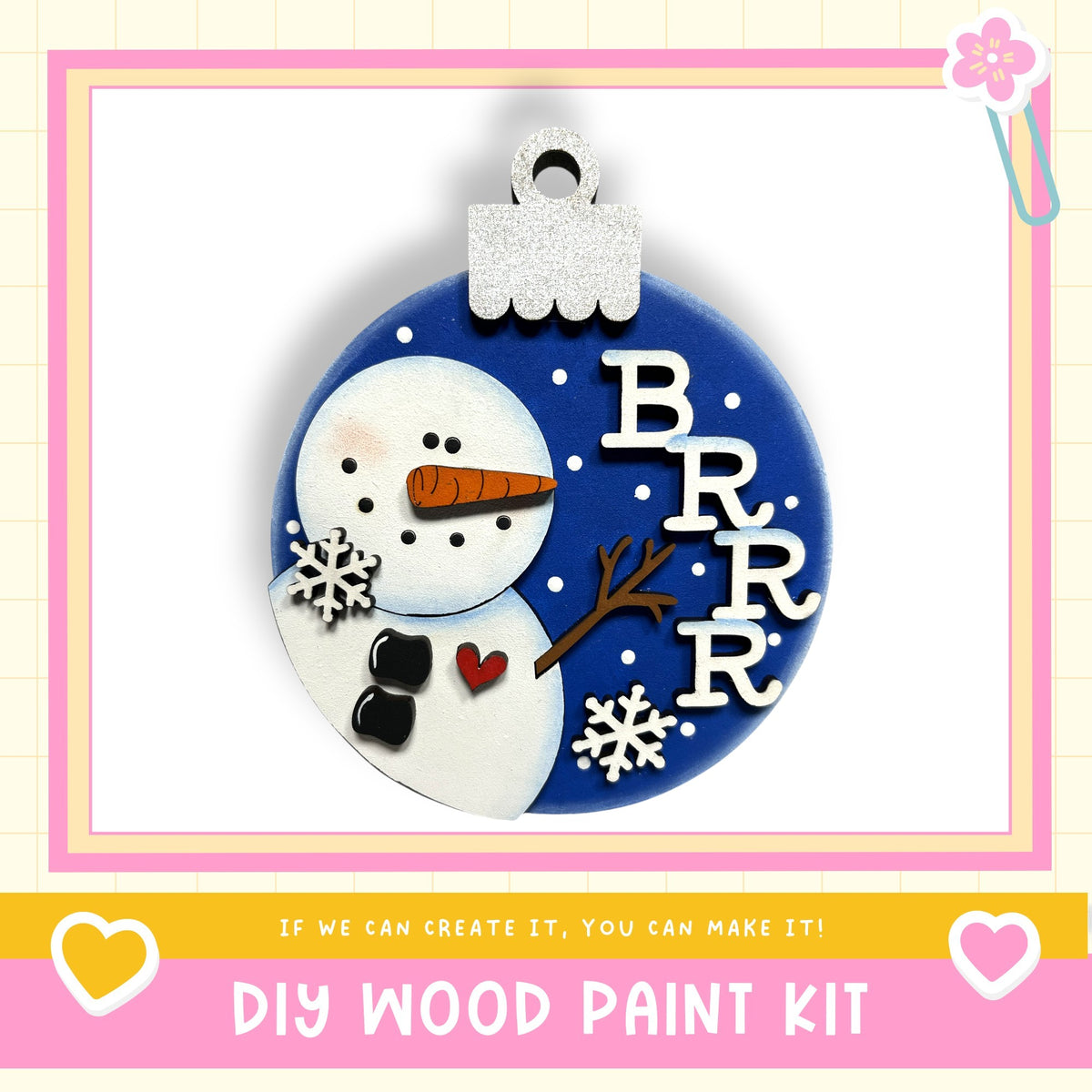 A snowman ornament with a blue background, white snowflakes, and a red heart. The ornament has the word "BRRR" written on it in white letters.