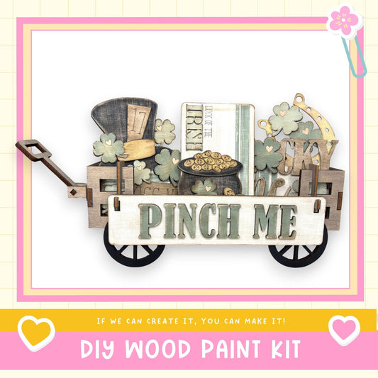 A wooden wagon with a sign that says "Pinch Me" and various other wooden objects, such as a hat, a book, and a clock, is displayed in the image.