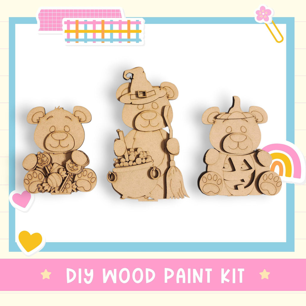three wooden bear figurines, each with a unique outfit or accessory, arranged in a row. The bears are depicted in a playful and whimsical manner, suggesting a DIY wood paint kit for creating similar bear-themed decorations or toys.