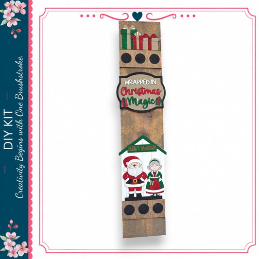a wooden sign with various Christmas-themed decorations, including a Santa Claus and an elderly couple, as well as a sign that says "wrapped in Christmas magic".