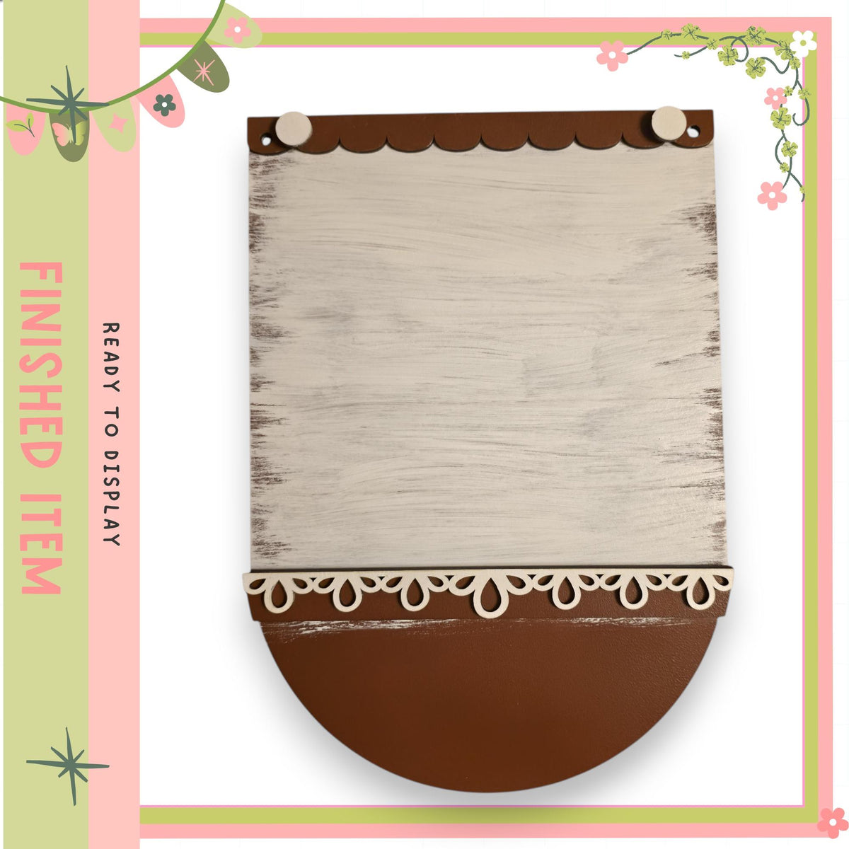 a wooden sign with a white background and decorative elements, such as lace trim, placed within a pink and green frame.