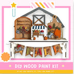 The image is a colorful and festive DIY wood paint kit for creating a fall-themed display. It includes a wooden house, a sign, and a banner that says "Hello Fall". The kit appears to be made of wood and is designed to be assembled and painted to create a seasonal decoration.