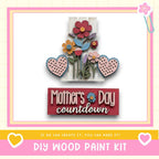 The image is a colorful and decorative Mother's Day countdown sign, featuring a variety of flowers and hearts in shades of pink, blue, and yellow. The sign is framed by a pink border and includes the text "Mother's Day countdown" and "DIY WOOD PAINT KIT" along with a heart symbol.