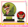 two wooden snow globes, each containing a reindeer. The snow globes are set against a green background, and the text below the image encourages viewers to create their own DIY wood paint kit.