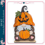 A wooden gnome figure with a carved pumpkin on its head, wearing a brown outfit and holding a pumpkin.