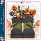 A Halloween-themed DIY kit featuring a pair of green monster boots with various spooky and festive decorations, including a jack-o-lantern, candy corn, and a ghost.