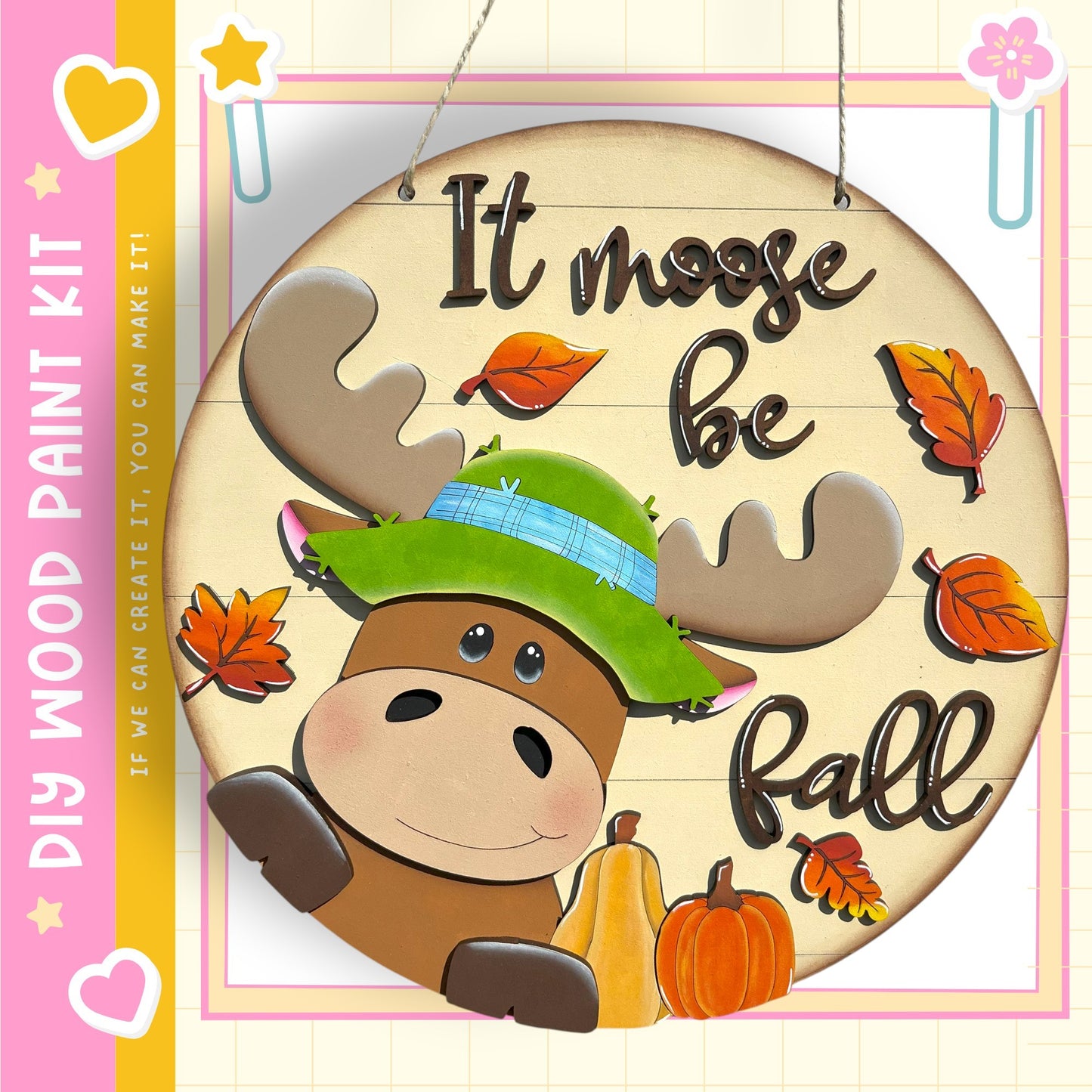 A wooden sign featuring a cartoon moose wearing a green hat and surrounded by autumn leaves and pumpkins, with the text "It moose be fall" displayed on it.