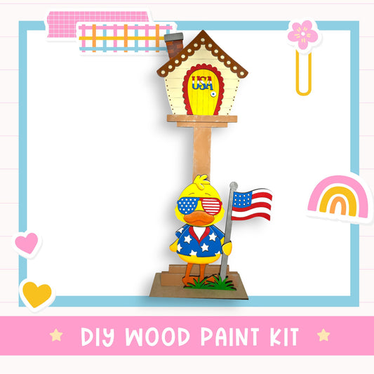 A DIY wood paint kit featuring a cartoon duck holding an American flag, with a colorful house and other decorative elements in the background.