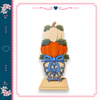 A decorative arrangement of three stacked pumpkins, each with a blue ribbon bow, placed on top of a blue and white vase.