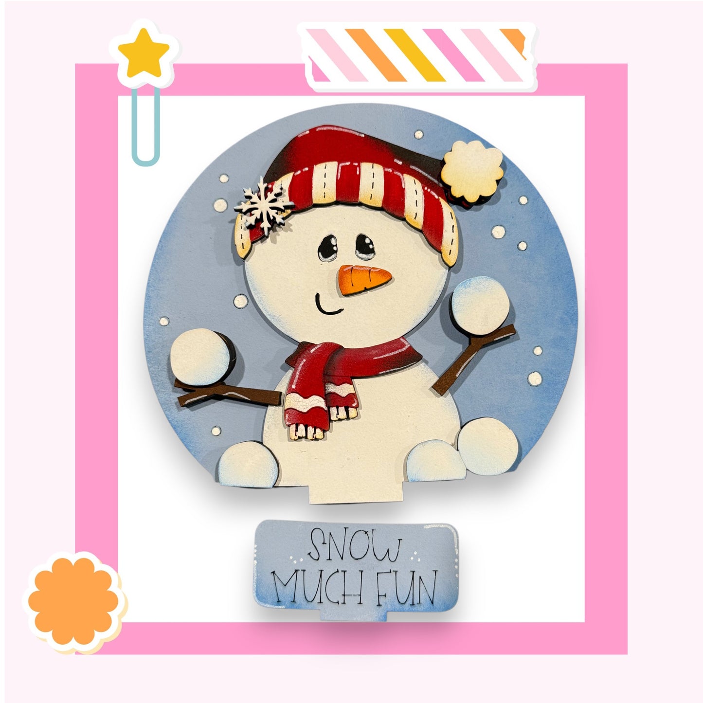 A snowman wearing a red and white striped hat and scarf, with a carrot nose and two snowballs, is depicted against a blue background with a pink border.
