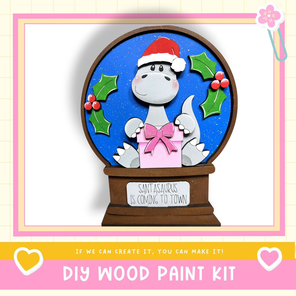 A wooden snow globe with a cartoon dinosaur wearing a Santa hat and holding a gift box, surrounded by holly leaves and berries.