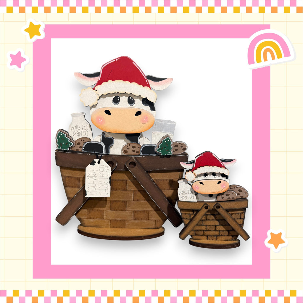 A wooden basket with two cow figurines inside, one larger and one smaller, wearing Santa hats. The basket is decorated with various items, including a sign that reads "Maid for a cause".