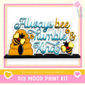 The image is a colorful and playful DIY wood paint kit featuring a beehive and two bees, along with the text "Always bee humbly & kind" and a heart symbol.