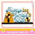 The image is a colorful and playful DIY wood paint kit featuring a beehive and two bees, along with the text "Always bee humbly & kind" and a heart symbol.