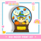 A DIY wood paint kit featuring a cartoon moose wearing a witch's hat and surrounded by autumn leaves and pumpkins, with a sign that says "FALLING FOR MOOSE SEASON".