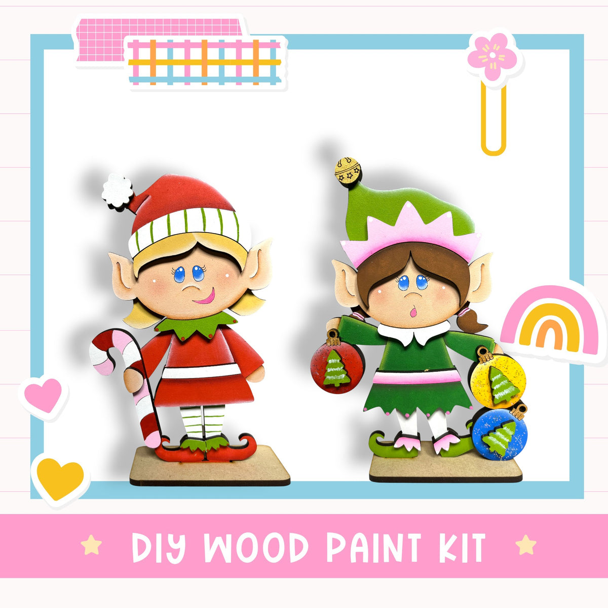 two wooden elf figurines, one wearing a red outfit and the other wearing a green outfit, holding Christmas ornaments. The image also includes a DIY wood paint kit and decorative elements such as hearts and a rainbow.