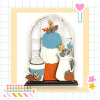 A wooden shelf with various fall-themed decorations, including a blue pumpkin, a white pitcher, a blue mug with whipped cream, and a white vase with a pumpkin. The shelf is set against a white background with a grid pattern.