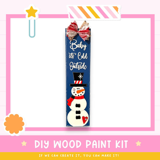 a DIY wood paint kit for creating a snowman, with a snowman decoration and a bow on a blue sign.