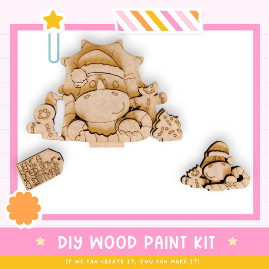 The image is a colorful and playful DIY wood paint kit featuring a variety of wooden shapes and characters, including a dinosaur, a cat, and a small elf. The kit appears to be designed for children to create their own wooden designs and characters.