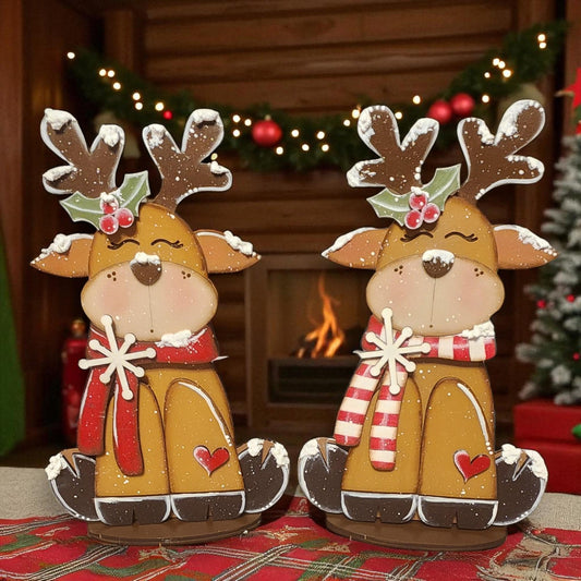 Two gingerbread reindeer figurines, each wearing a red scarf and antlers, are sitting on a plaid tablecloth in front of a fireplace decorated with Christmas lights.