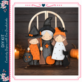 A Halloween-themed DIY kit featuring three wooden dolls dressed in witch costumes, each holding a different Halloween-themed prop, such as a broom, pumpkin, and cat.