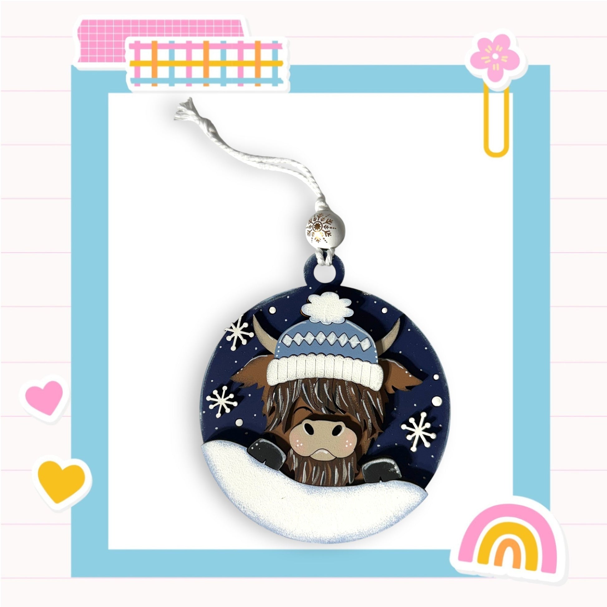 A decorative ornament featuring a cow wearing a winter hat and surrounded by snowflakes, with a colorful frame and various other decorative elements in the background.