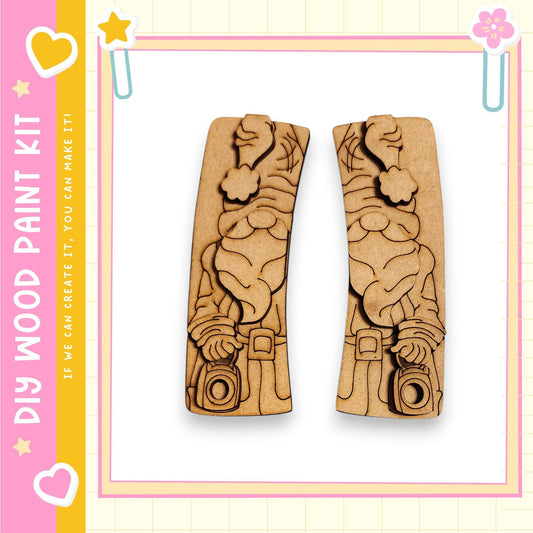 two wooden cutouts of a gnome holding a camera, set against a pink and yellow background with decorative elements.