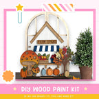 The image is a colorful and whimsical DIY wood paint kit, featuring a farm stand with a mushroom, pumpkins, and a tree, surrounded by a pink and white striped border. The kit appears to be made of wood and is designed for painting, with the text "DIY WOOD PAINT KIT" and "IF WE CAN CREATE IT, YOU CAN MAKE IT!" displayed.