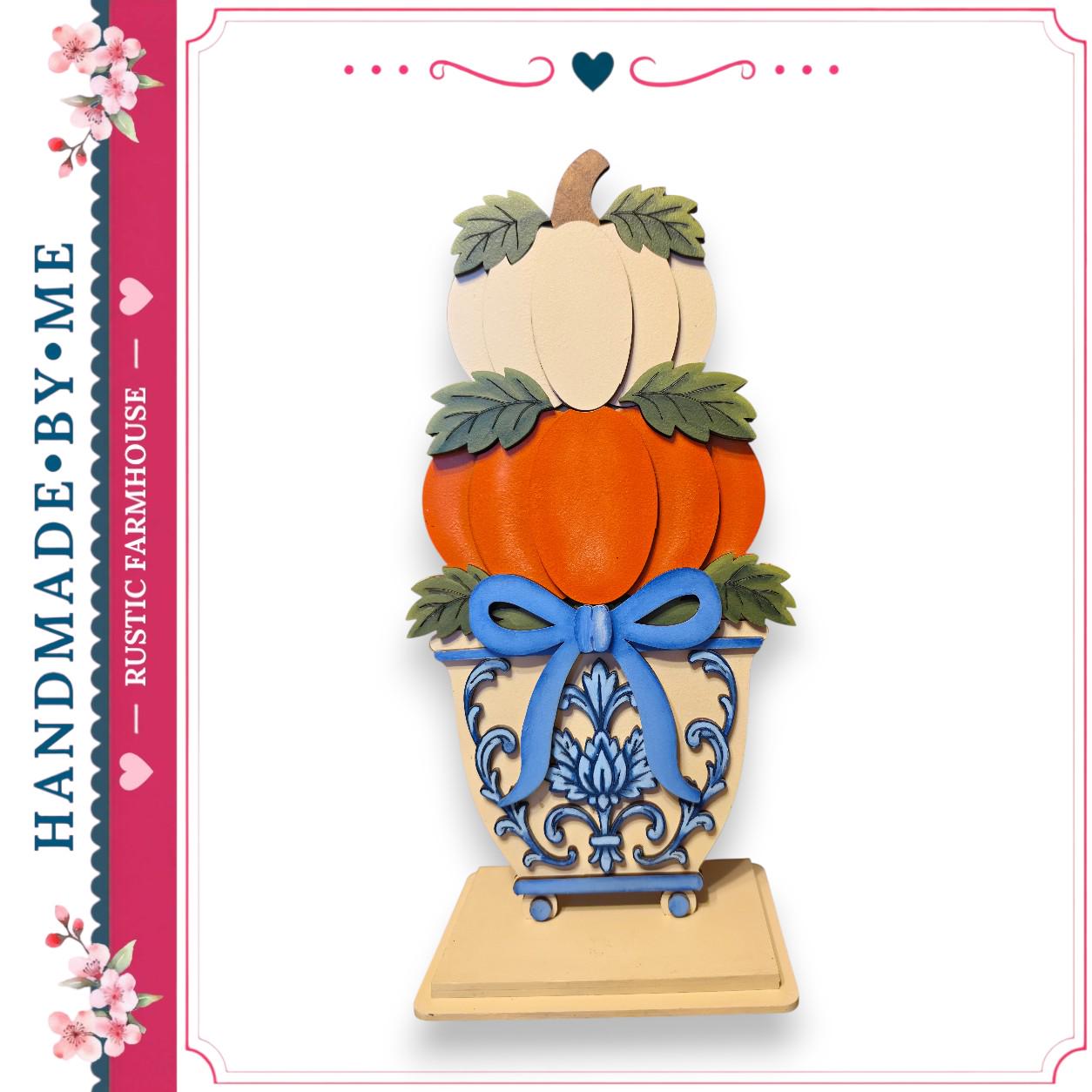 A hand-made wooden sculpture of a pumpkin and a blue bow, placed on a wooden base with a decorative design.